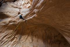 A rock climber rappels down a sandstone canyon wall, secured by a rope.