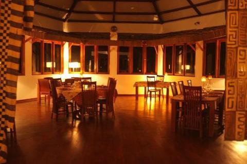 The image depicts the interior of a restaurant or dining area, featuring wooden tables and chairs arranged around the room, with natural light filtering through the windows, creating a warm and inviting ambiance.