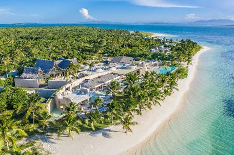 Aerial view of a luxurious beachfront resort nestled amongst lush tropical foliage on a beautiful island, with a pristine white sand beach meeting crystal-clear turquoise waters.