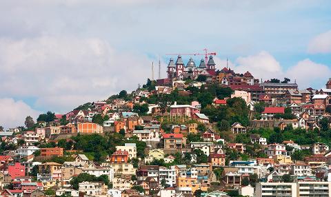A hillside is densely packed with colorful buildings, topped by a unique domed structure and a construction crane.