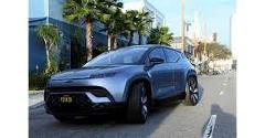 Here's a description of the image:A blue Fisker Ocean electric SUV is parked on a street with palm trees and buildings in the background.