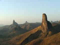 Here's a one-sentence description of the image:The image showcases a landscape with several prominent rock formations rising above a rugged, hilly terrain, bathed in warm sunlight under a clear sky.