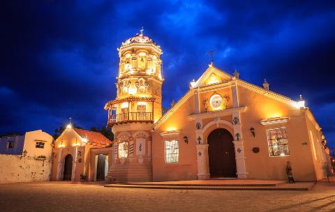 Mompox & Aracataca Cultural Journey (3 Days / 2 Nights) A brightly lit colonial church with a tall bell tower stands against a dramatic blue night sky in Mompox, Colombia.