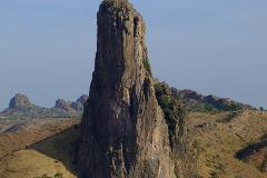 A tall, imposing rock formation dominates the landscape, set against a backdrop of rolling hills and a clear blue sky.