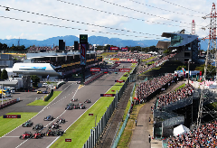 A high-angle shot captures the excitement of a Formula 1 race, with a pack of cars speeding along the track lined by cheering crowds and Lenovo ads.