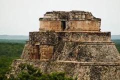 Here's a description of the image:The image shows a multi-tiered Mayan pyramid or temple, likely located in Uxmal, featuring intricate stonework and design, set against a backdrop of dense green forest.