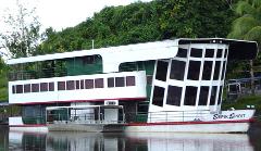 Ein dreistöckiges, grün-weißes Kreuzfahrtschiff mit eckigen Fenstern namens „Sepik Spirit“ liegt an einem Fluss, umgeben von üppigen grünen Bäumen.