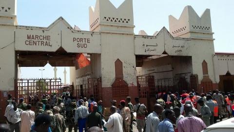 A crowd of people, including some in military uniforms, gather in front of an arched entranceway labeled "MARCHE CENTRAL" and "PORTE SUD".
