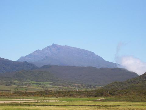 A wide shot of Piton de la Fournaise, a volcano on Reunion Island, with a partly cloudy sky.