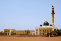 Here's a description of the image:A mosque with a tall minaret and a green dome stands against a clear blue sky, showcasing its Islamic architecture.