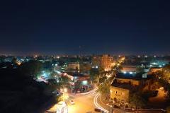 Here's a description of the image:The image shows a nighttime view of a city, possibly Niamey, with buildings illuminated by streetlights and a dark sky above.