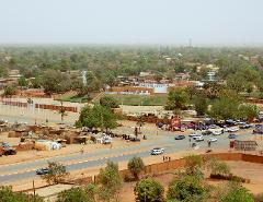 An aerial view of Agadez, Niger, with buildings, trees, roads, and bustling street life under a hazy sky.