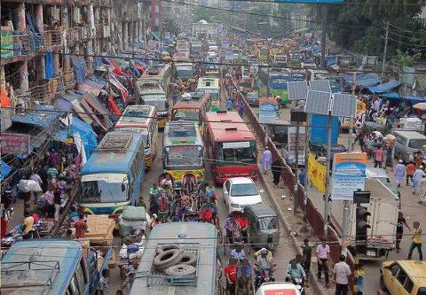 3-Day Dhaka Heritage & Culture Tour — Old Palaces, Lost Cities & Zamindari Mansions A congested street in Dhaka is filled with buses, cars, and motorcycles, with a busy marketplace and buildings lining the road.