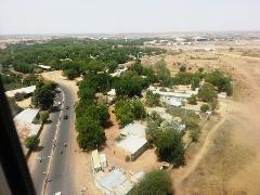 An aerial view captures a sprawling landscape, blending urban and rural elements with a road, buildings, trees, and an airport in the distance.