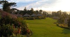 The image showcases a scenic view of Ambua Lodge, featuring traditional thatched-roof huts nestled amidst lush greenery and rolling hills, with a serene and tranquil atmosphere.