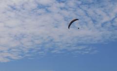 A paraglider soars through a sky filled with fluffy white clouds against a blue background.