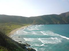 Tayrona Park Day Tour A scenic view of a coastline with gentle waves lapping at the sandy beach, framed by verdant hills.
