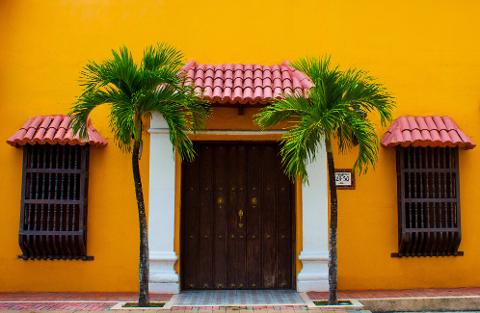 Cali City Tour A vibrant yellow building with a dark wooden door and windows, adorned with small palm trees and red tiled awnings.