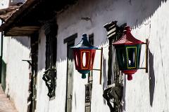 Two colorful, lantern-like wall lamps decorate a white building with dark windows and a partially visible roof with brown tiles.