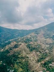 An aerial view shows a mountainous landscape dotted with buildings under a cloudy sky.