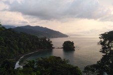 Darien Gap, Rainforest, and Culture from Panama Certainly! Here's a description of the image in one sentence:The photo shows a serene coastal scene with a small, vegetated island in the calm bay, surrounded by lush green hills and forests under a cloudy sky.