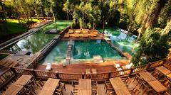 An expansive outdoor leisure area features a multi-tiered pool system, wooden lounge decks, and a restaurant terrace nestled among lush greenery.