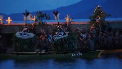 The image shows men in a boat wearing traditional masks, with the word "TATABU" printed on the boat's side, possibly taken during the Rabaul Mask Festival.