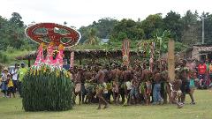 A group of people in traditional clothing and headdresses are gathered in a field, possibly for a festival or celebration, in Papua New Guinea.