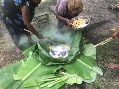 Rabaul Day Tour Women prepare a traditional meal cooked with hot stones and vegetables wrapped in banana leaves, a common practice in Rabaul, Papua New Guinea.