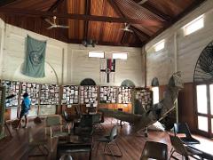 The image shows an interior shot of a museum in Papua New Guinea with flags and exhibits, including the wreckage of a plane and various pictures.