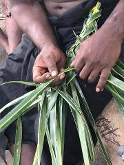Close-up shot of a person weaving green palm fronds, likely for a traditional craft or basket making.