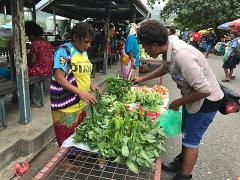 A woman in a yellow shirt shops for fresh greens at an outdoor market in Rabaul, Papua New Guinea.