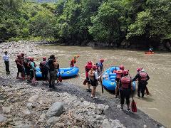 A group of people with red helmets and life vests is preparing for a rafting trip on a river.