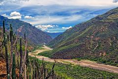 A picturesque view of a river winding through a valley framed by lush green mountains under a cloudy sky.