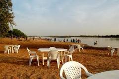 A sandy beach scene with white plastic tables and chairs near a body of water and people enjoying themselves in the distance.