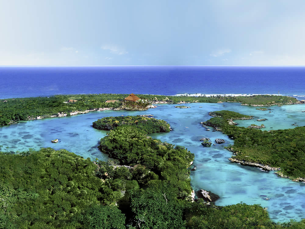 Riviera Maya Airplane Tours A vibrant, high-angle view showcases the Riviera Maya with lush green islands, turquoise water, and the distant ocean under a clear blue sky.
