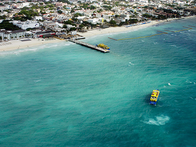 Riviera Maya Airplane Tours An aerial view of a coastal town, featuring a pier, beach, and turquoise ocean with boats, showcasing the Riviera Maya's beauty.