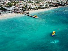 Riviera Maya Airplane Tours An aerial view of a coastal town, featuring a pier, beach, and turquoise ocean with boats, showcasing the Riviera Maya's beauty.