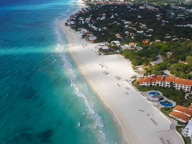Riviera Maya Airplane Tours An aerial shot of the Riviera Maya shoreline features turquoise water, a pristine white sand beach, and lush green vegetation interspersed with beachfront properties and resorts.