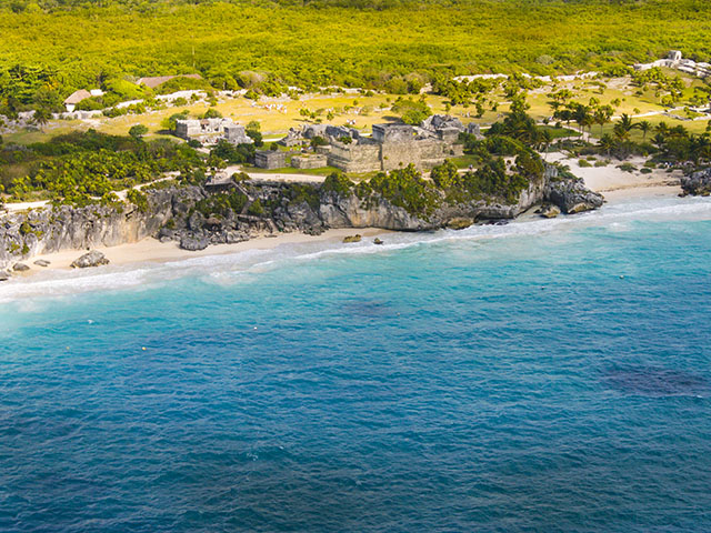 Riviera Maya Airplane Tours Aerial view of the Tulum archaeological site on the Riviera Maya, with ancient ruins perched on a cliff overlooking the turquoise Caribbean Sea.