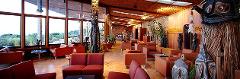 Rondon Ridge (Mt. Hagen) This image shows a spacious lobby with red and orange seating areas, large windows overlooking green scenery, and intricate tribal art pieces throughout the room.