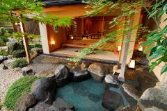露天風呂には、石で縁取られたプール、豊かな緑、木製のポーチのある伝統的な日本建築が備わります。