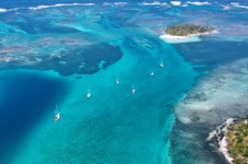 Panama City and San Blas Here's a description of the image:An aerial view shows several sailboats navigating through a turquoise channel surrounded by coral reefs and small islands, with varying shades of blue in the water.