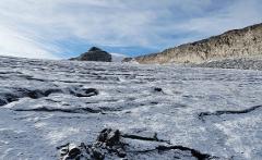 A snowy landscape with a mountain peak and a rocky cliff under a blue, streaked sky.