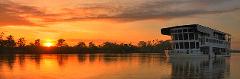 Sepik Spirit (Board from Karawari – Cruise Ship) A panoramic shot shows a cruise ship named "Sepik Spirit" on calm water with a vibrant orange sunset and silhouetted trees in the background.