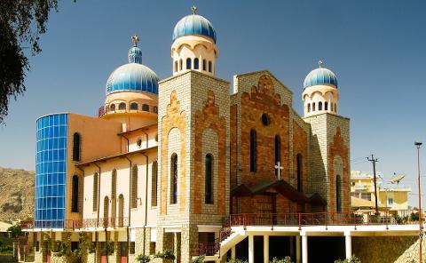 This is an eye-level shot of the St. Michael’s Orthodox Church in Asmara, Eritrea, featuring three blue-domed towers, a brick facade, and modern glass windows.