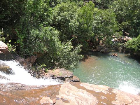 2 Day Bamako – Siby Cultural Escape A waterfall cascades over rocks into a serene turquoise pool surrounded by lush green trees.