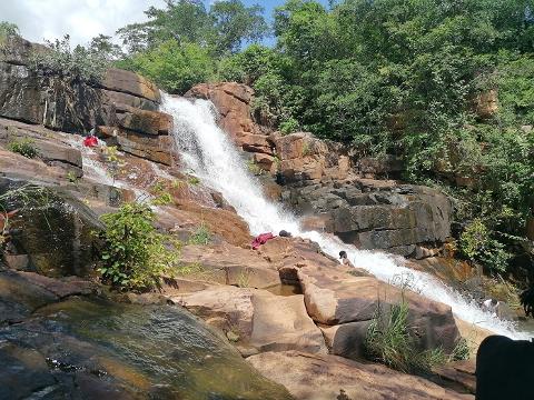 Full Day Tour To Siby And Bamako People are enjoying themselves at a beautiful waterfall with lush green trees and rocky terrain.
