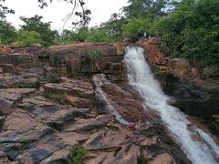 Full Day Tour To Siby And Bamako A powerful waterfall cascades over rugged, rocky terrain, surrounded by lush green foliage.