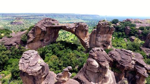 Full Day Tour To Siby And Bamako A natural rock arch frames a lush green valley dotted with trees, with rugged cliffs and distant hills under a bright sky.